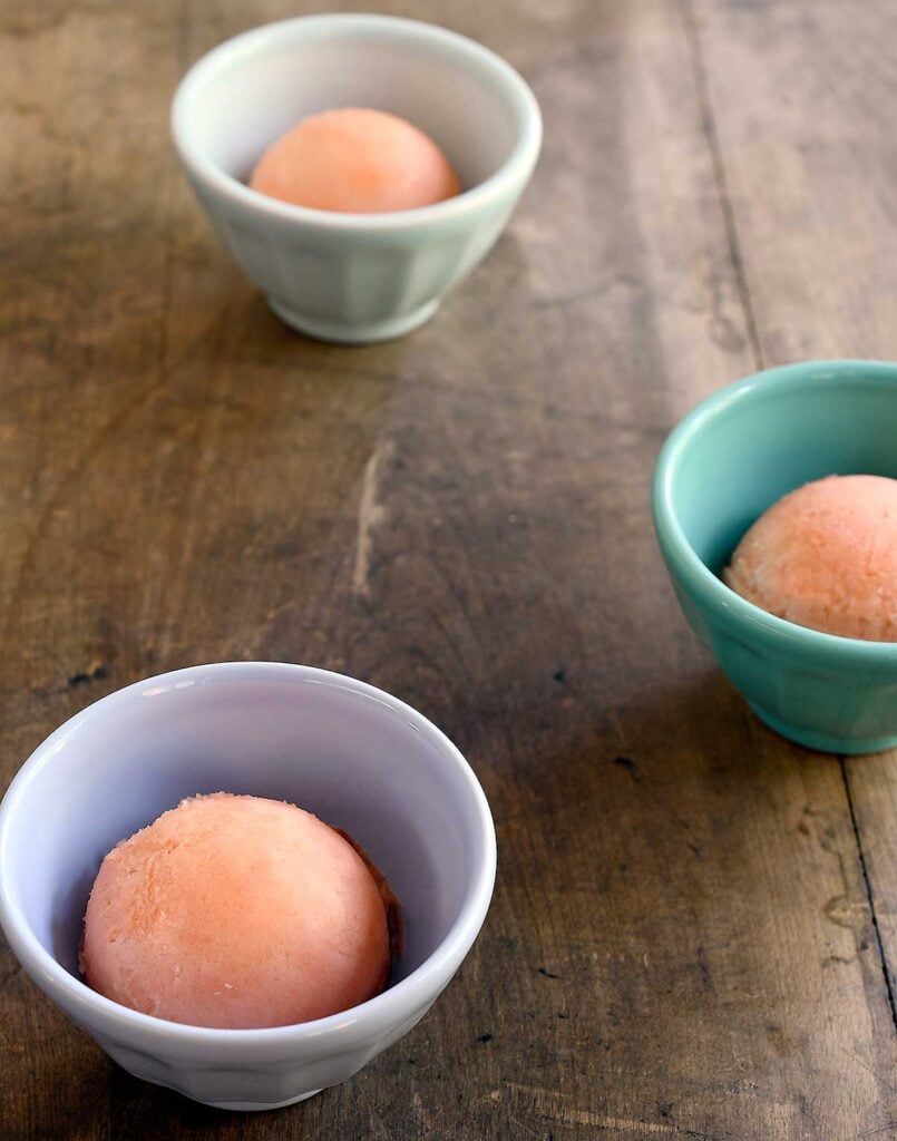 Scoops of watermelon sorbet in small cups on a wooden table.