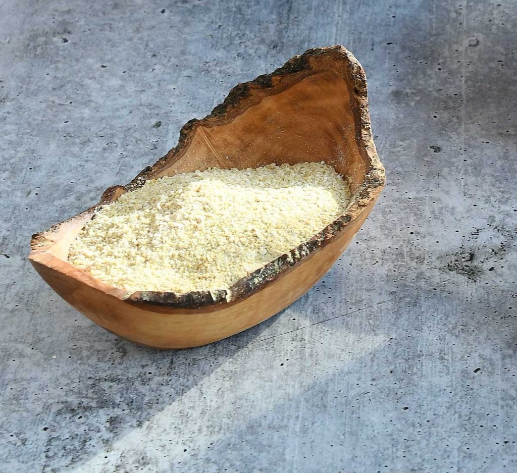 Nut free vegan parmesan in a wooden bowl on a grey concrete counter.