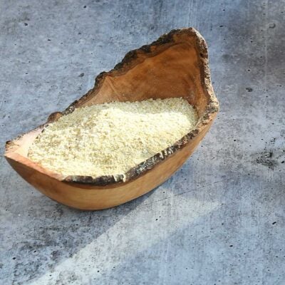 Nut free vegan parmesan in a wooden bowl on a grey concrete counter.
