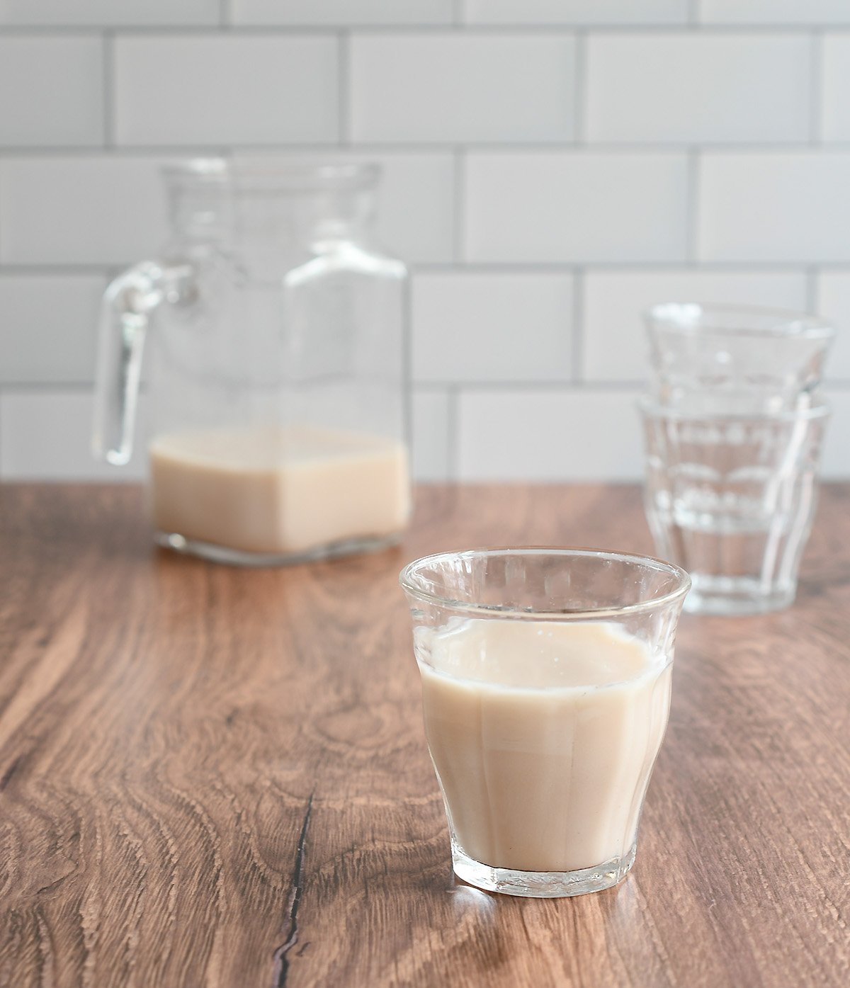 Glass of freshly made pecan milk with a pitcher and other glass on a wooden counter.