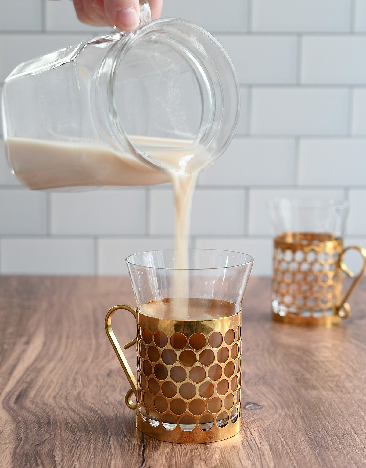 Pecan milk pouring from a glass pitcher into a gold and glass coffee cup.