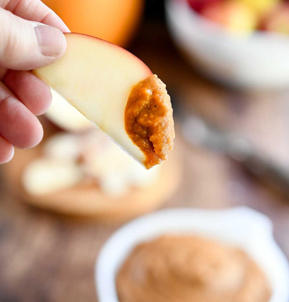 An apple slice dipped into the pumpkin dessert hummus.