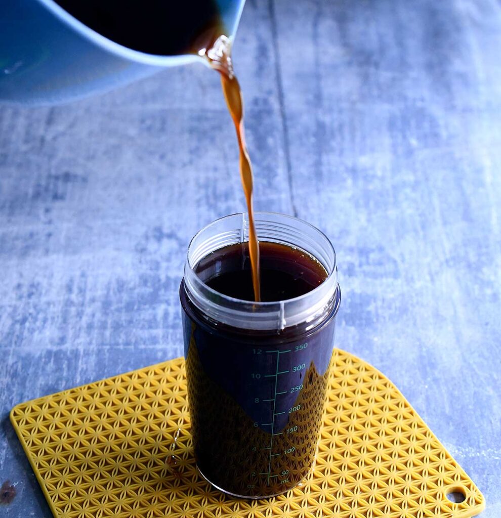 Strained vegan pumpkin spice syrup pouring into an OXO salad dressing container