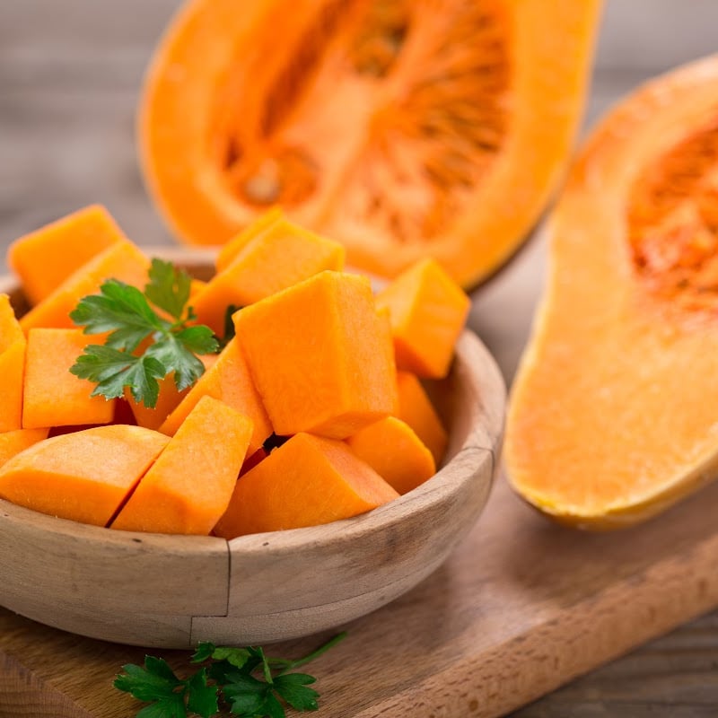 butternut squash cut in cubes in wooden mini bowl and butternut squash cut in half beside it