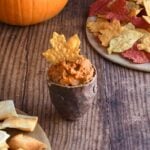Ancho chile pumpkin hummus in a brown handforn potter bowl with a maple leaf shaped yellow tortilla chip