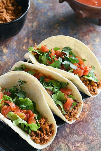 Soft tacos with minced soy curl filling topped with lettuce, chopped tomatoes, and cilantro.