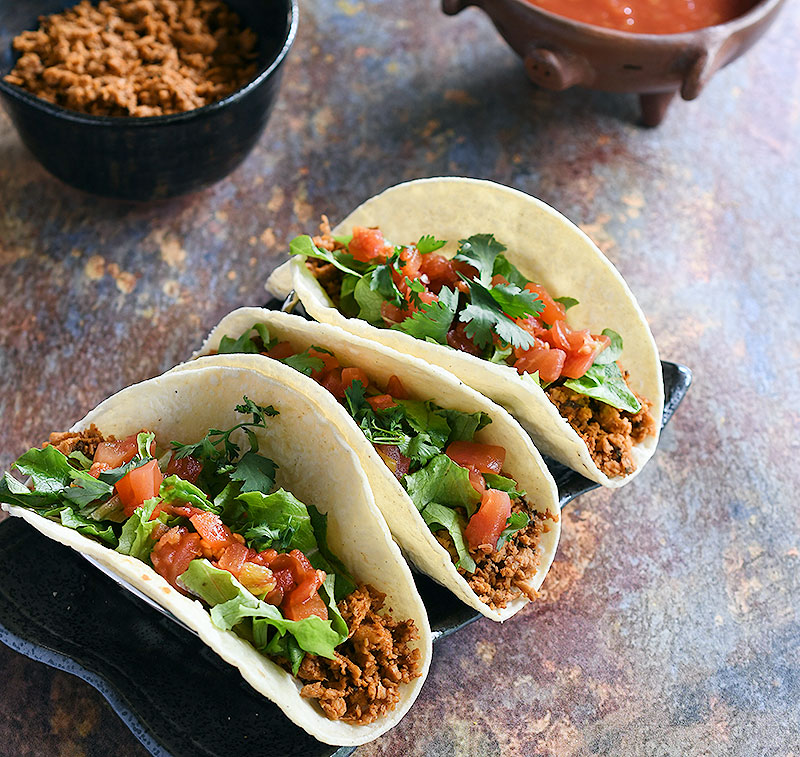 Soft tacos with minced soy curl filling topped with lettuce, chopped tomatoes, and cilantro.