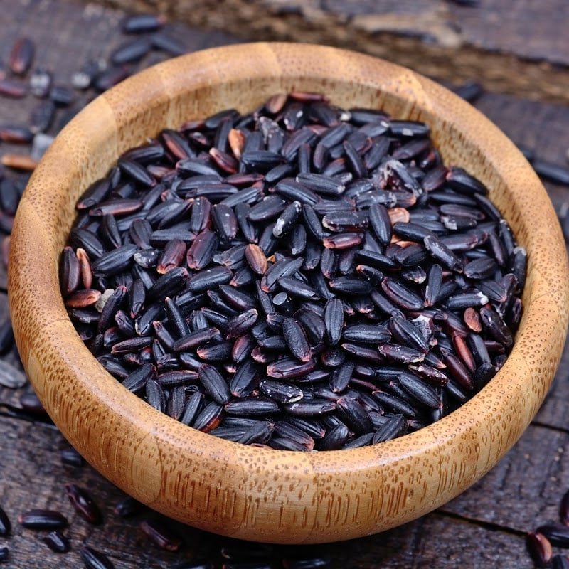 Forbidden rice in wooden bowl on top of wooden table