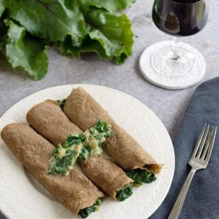 3 gluten-free teff crepes on a white plate with a fork and a wine glass on the side