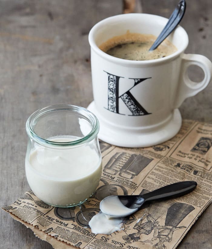 Coconut Oat Vanilla Nut Vegan Coffee Creamer in a glass next to a mug with coffee