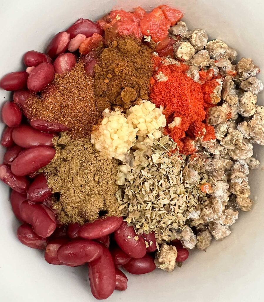 Beans, vegan crumbles, diced tomatoes, green chilies, garlic, and spices in a white crockpot.