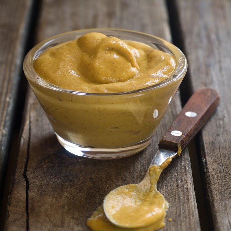 Dijon Mustard in a small saucer and teaspoon on top of a wooden table