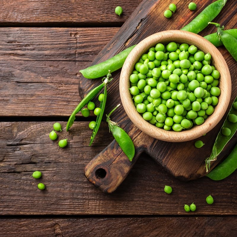 Grean Peas in wooden bowl on top of wooden table