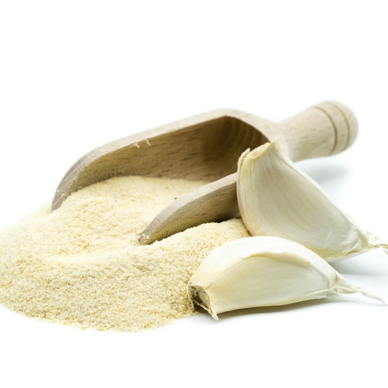 Granulated garlic in a wooden scoop with two whole cloves of garlic