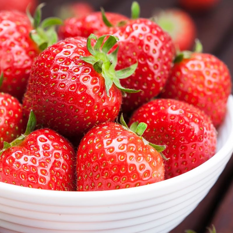 A bowl of fresh strawberries on wooden background